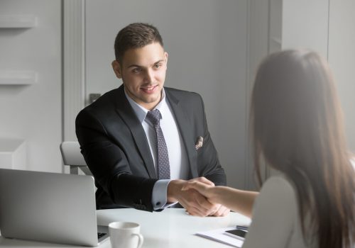 Friendly,Smiling,Businessman,And,Businesswoman,Handshaking,Over,The,Office,Desk